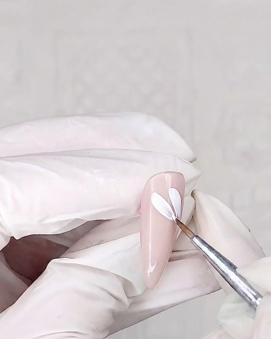 Ein Detailpinsel malt weiße Blütenblätter auf den rosa Nagel.