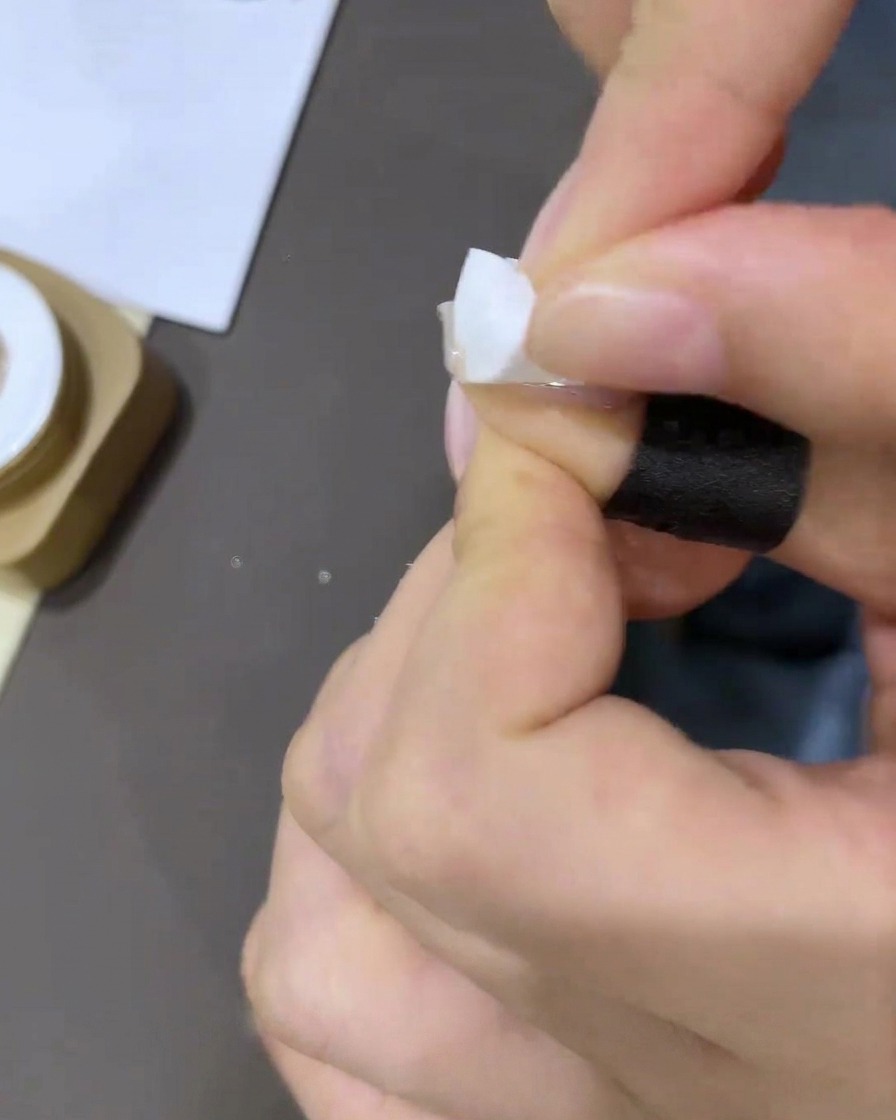 Nahaufnahme einer Hand, die ein kleines Stück weißes Concealer-Tape an die Basis der Nagelhaut anbringt.