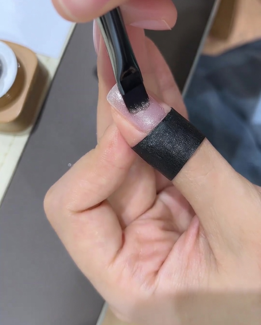Eine Hand benutzt einen Nagelmagneten über einem frisch lackierten Gelnagel, um die Glitzerpartikel zu bewegen.