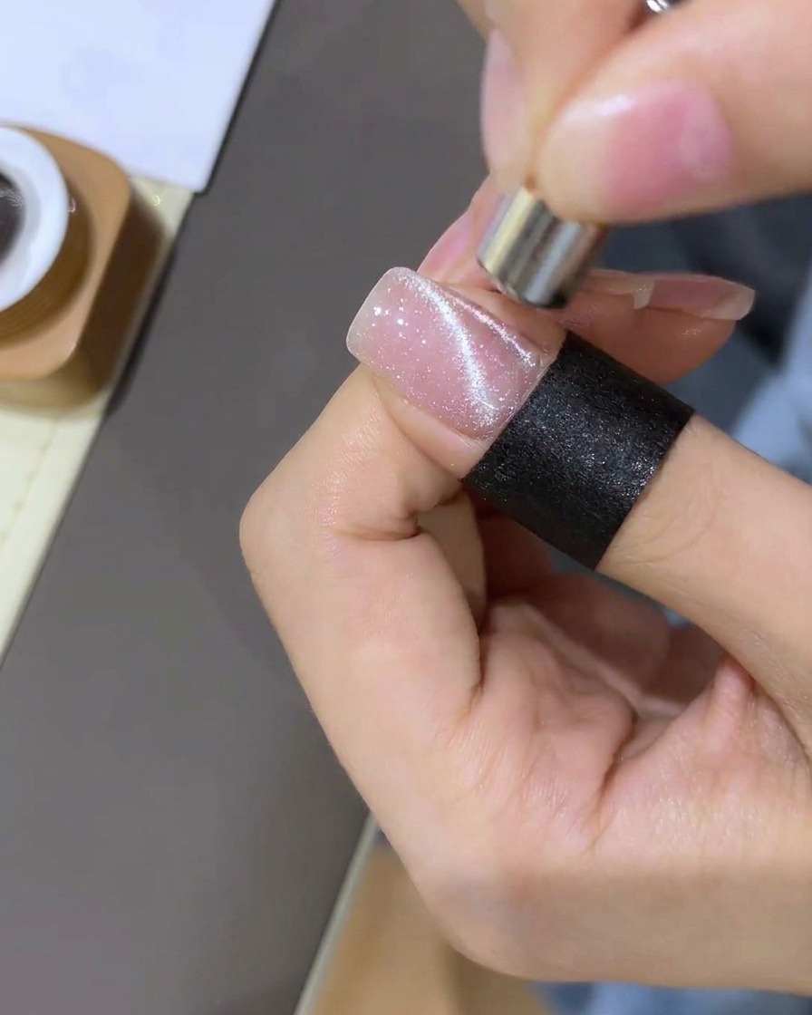 Eine Nahaufnahme zeigt, wie ein Magnet verwendet wird, um magnetischen Glitzer zu einer konzentrierten, kugelförmigen Form auf dem Nagel zu ziehen.