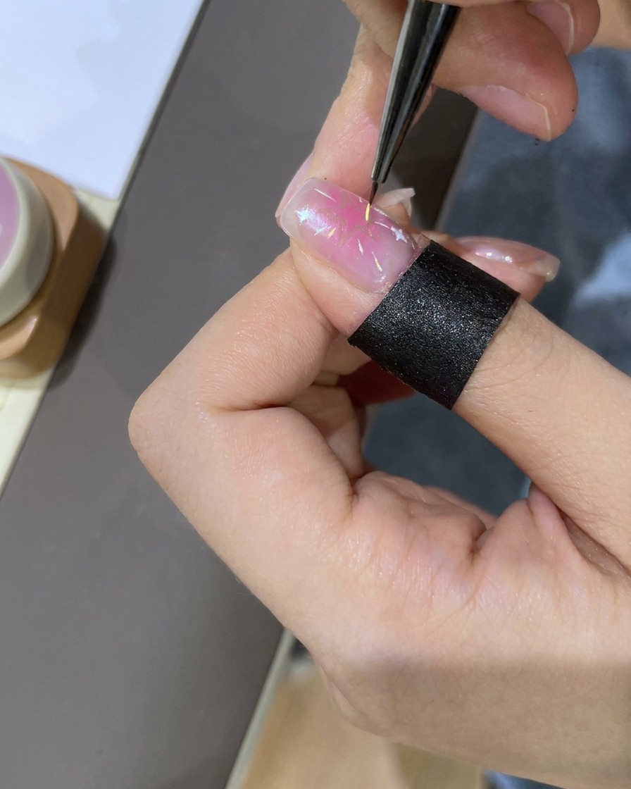 Ein Dotting-Tool wird verwendet, um kleine, bunte Akzente um den sternverzierten Nagel zu platzieren.