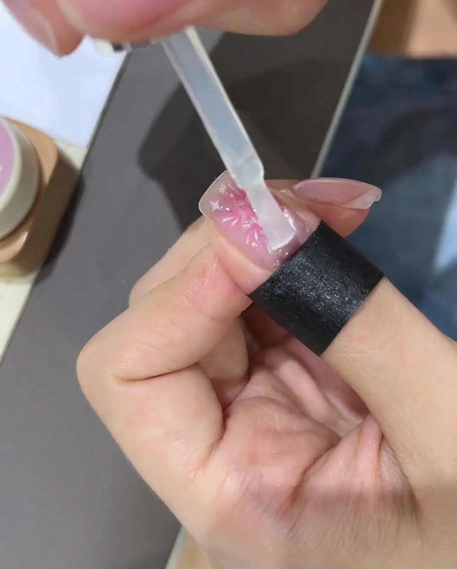 Ein Pinsel trägt einen klaren Top Coat über das fertiggestellte Stern-Nageldesign auf.