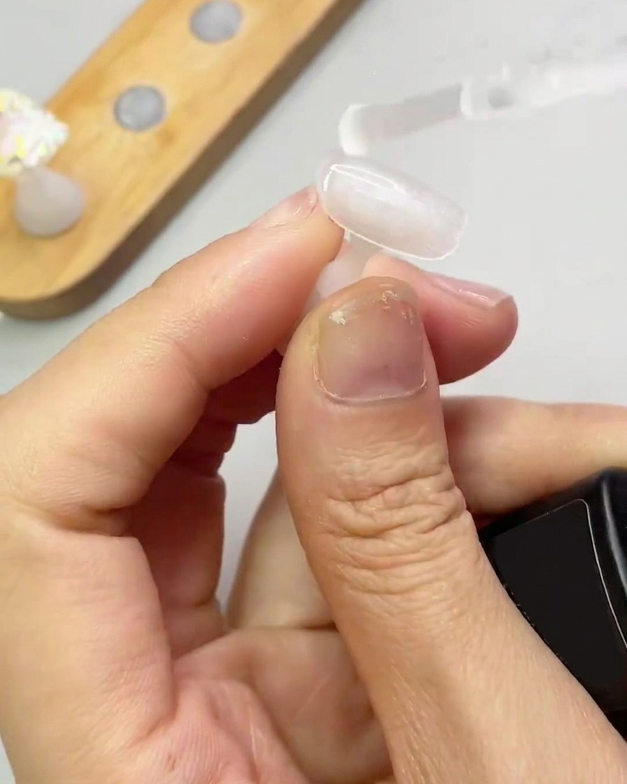 Ein Pinsel trägt eine dünne, klare Schicht Verstärkungsgel auf eine Nagelspitze auf.