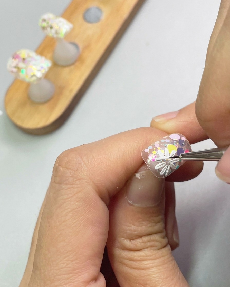 Nahaufnahme eines Pinsels, der weißes Modellage-Gel zu einer zweiten Gänseblümchen-Blüte formt.