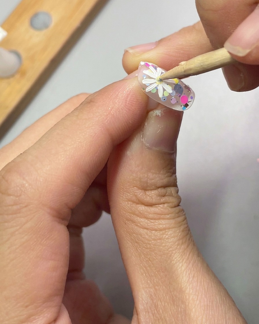 Ein Dotting-Tool platziert einen kleinen gelben Geltropfen in die Mitte eines 3D-Gänseblümchens.