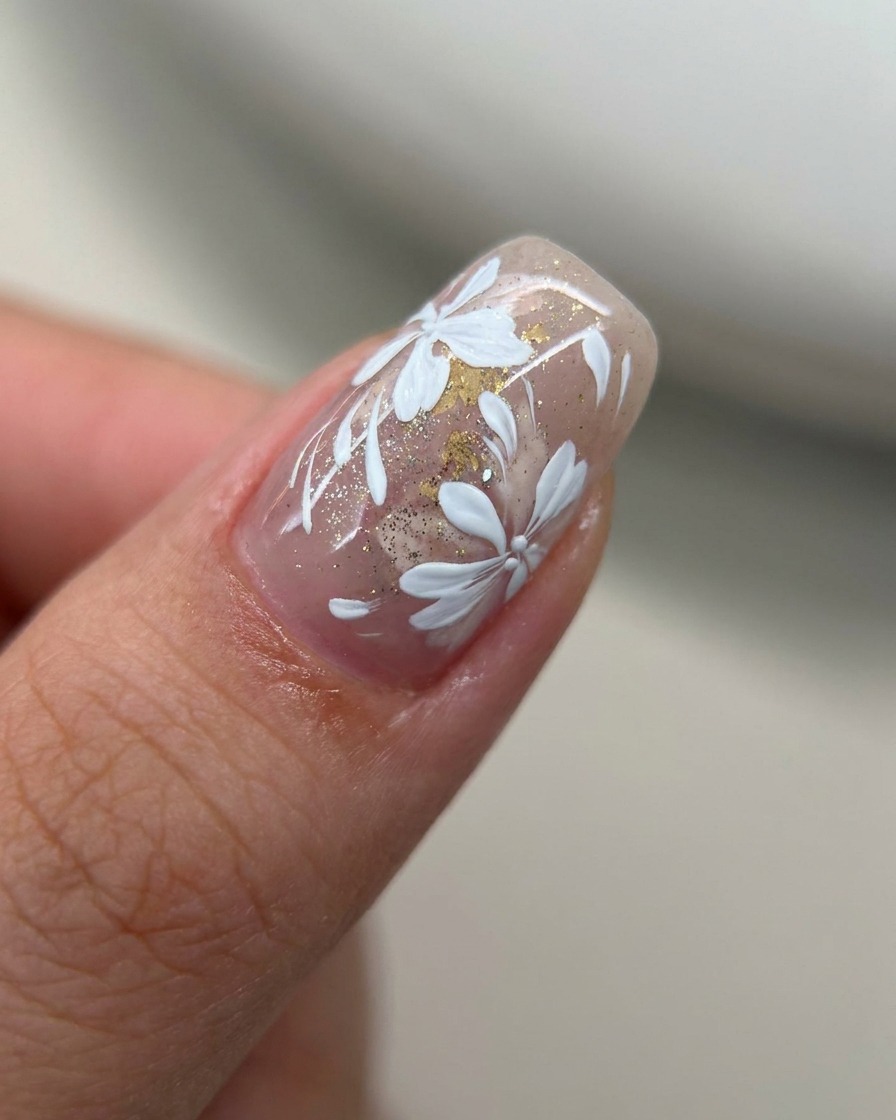 Nahaufnahme eines Nagels mit einem transparenten Nude-Pink-Tint, der mit einem Pinsel eine Schicht Goldglitzer erhält.