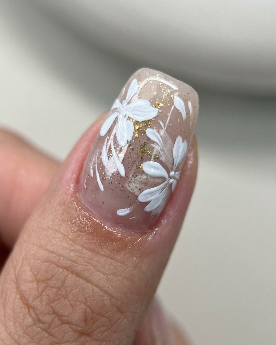 Ein Pinsel trägt klaren Top Coat über einen Nagel mit floraler Kunst und Goldakzenten auf.