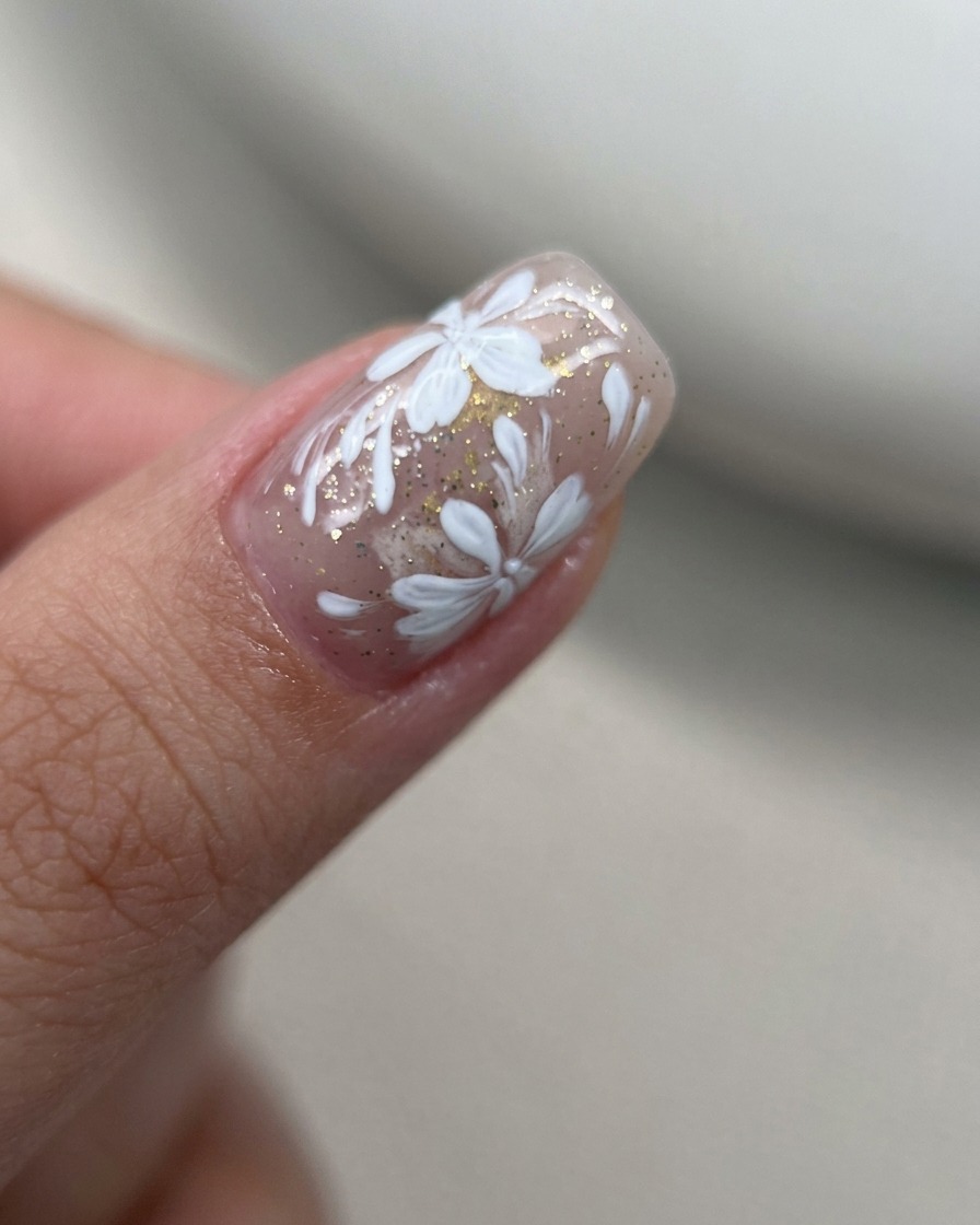 Makroaufnahme von weißen Gel-Blütenblättern, die in einem dichten Cluster auf einer Nude-Nageloberfläche gemalt werden.