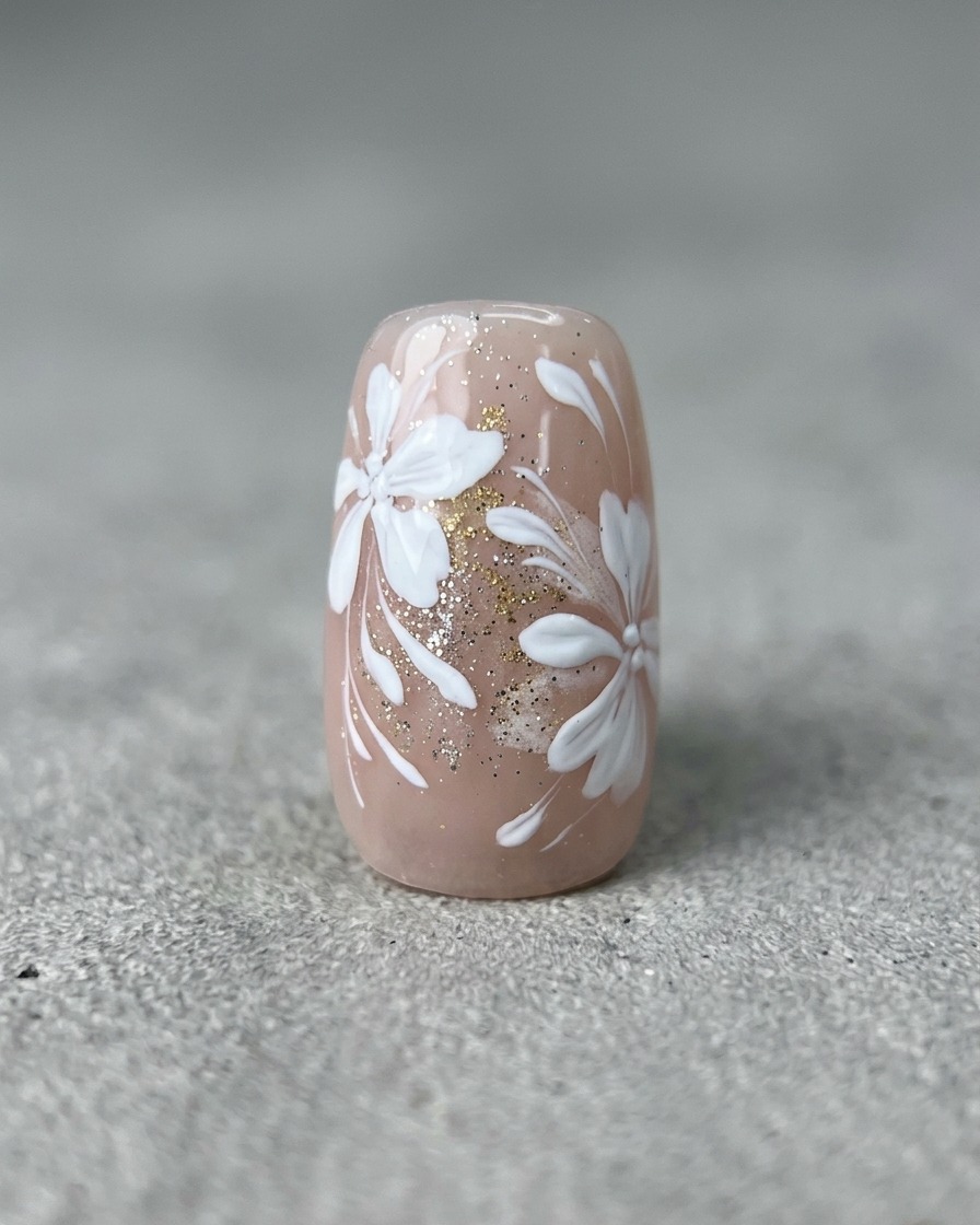 Ein feiner Liner-Pinsel zieht dünne, geschwungene weiße Linien auf einen Nagel mit fertigem Blumen- und Golddesign.