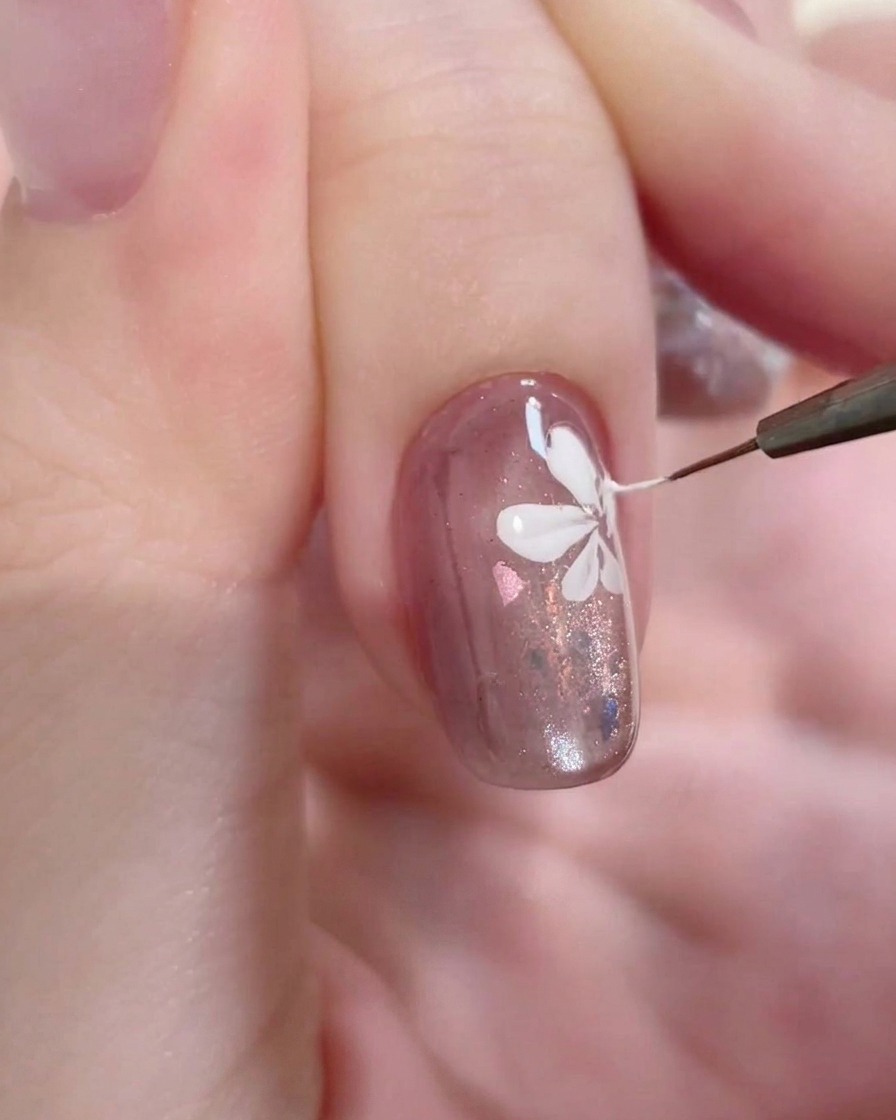 Eine Makroaufnahme eines feinen Liner-Pinsels, der einen präzisen weißen Strich in die Mitte einer gemalten Blume auf einem gelbeschichteten Nagel setzt.
