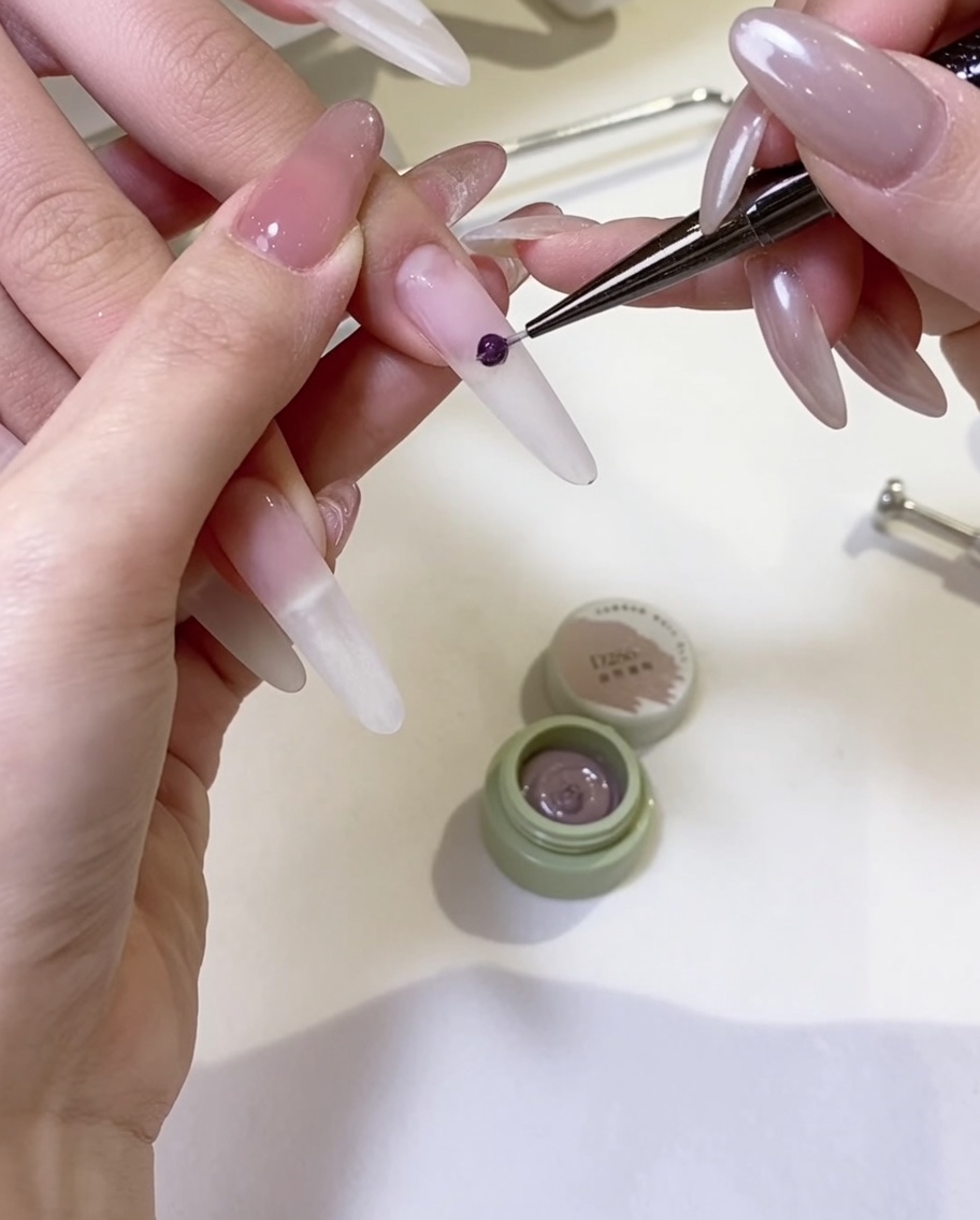 Ein Gelpinsel trägt eine gleichmäßige Schicht nudefarbenen Gellacks auf einen Nagel auf.