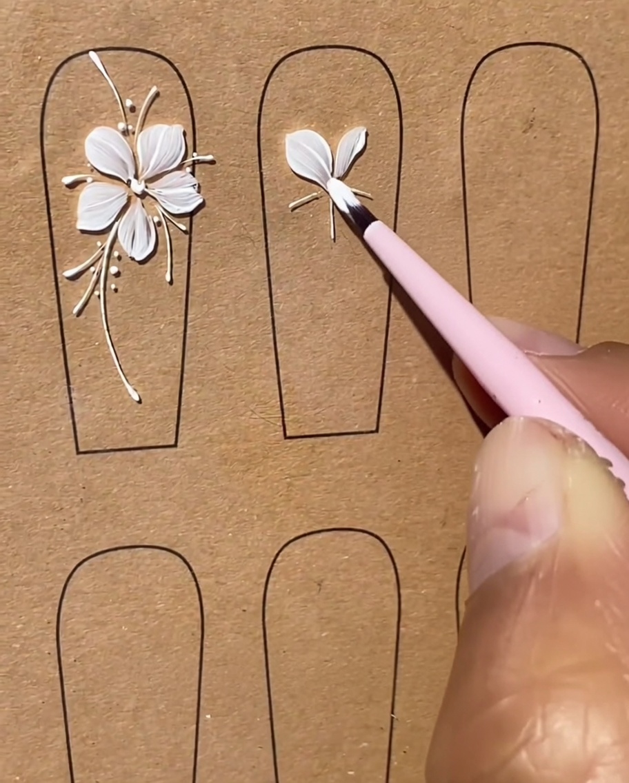 Ein Pinsel formt präzise ein drittes weißes Gel-Blütenblatt als Teil des Fünf-Blütenblatt-Designs.