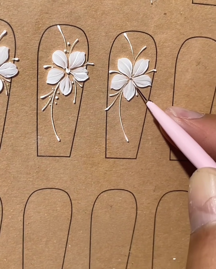 Ein Detailfoto zeigt kleine weiße Punkte, die als Highlights entlang der Linien eines floralen Nageldesigns aufgetragen werden.