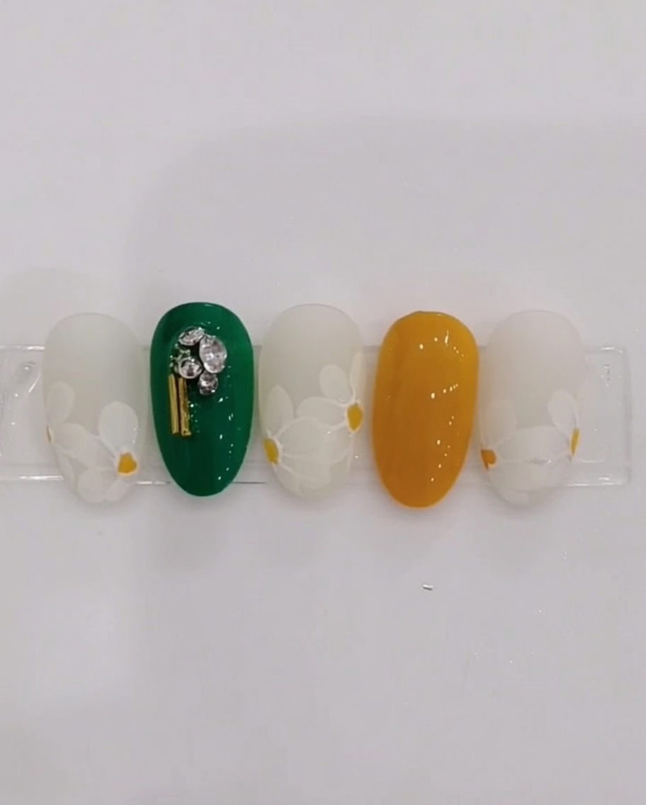 Ein feiner Detailpinsel platziert einen gelben Punkt in der Mitte eines Nagels.