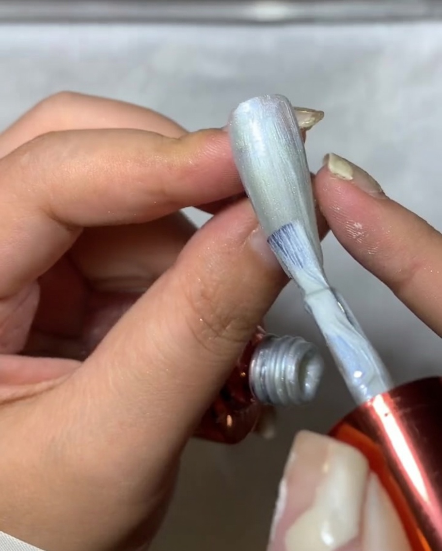 Nahaufnahme eines Pinsels, der silbernes Spider-Gel auf einen Nagel aufträgt und feine, netzartige Linien erzeugt.