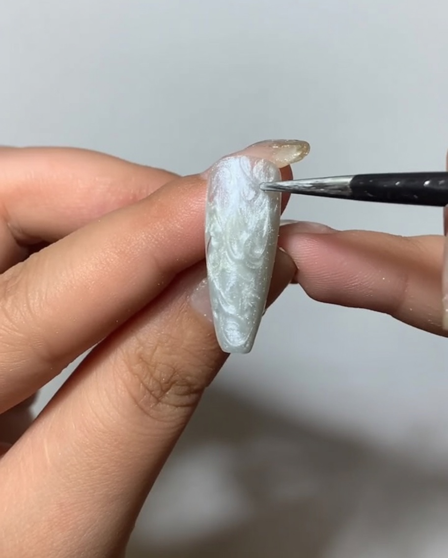 Ein Pinsel trägt ein klares mattes Top Coat auf einen texturierten, silbernen Spider-Gel-Nagel auf.