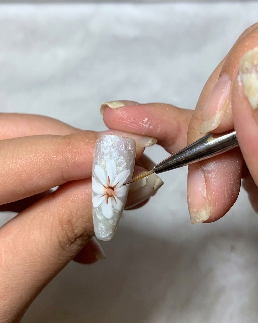 Ein feiner Pinsel trägt dickflüssiges, klares Gel über das weiße Blüten-Design auf, um Dimension aufzubauen.