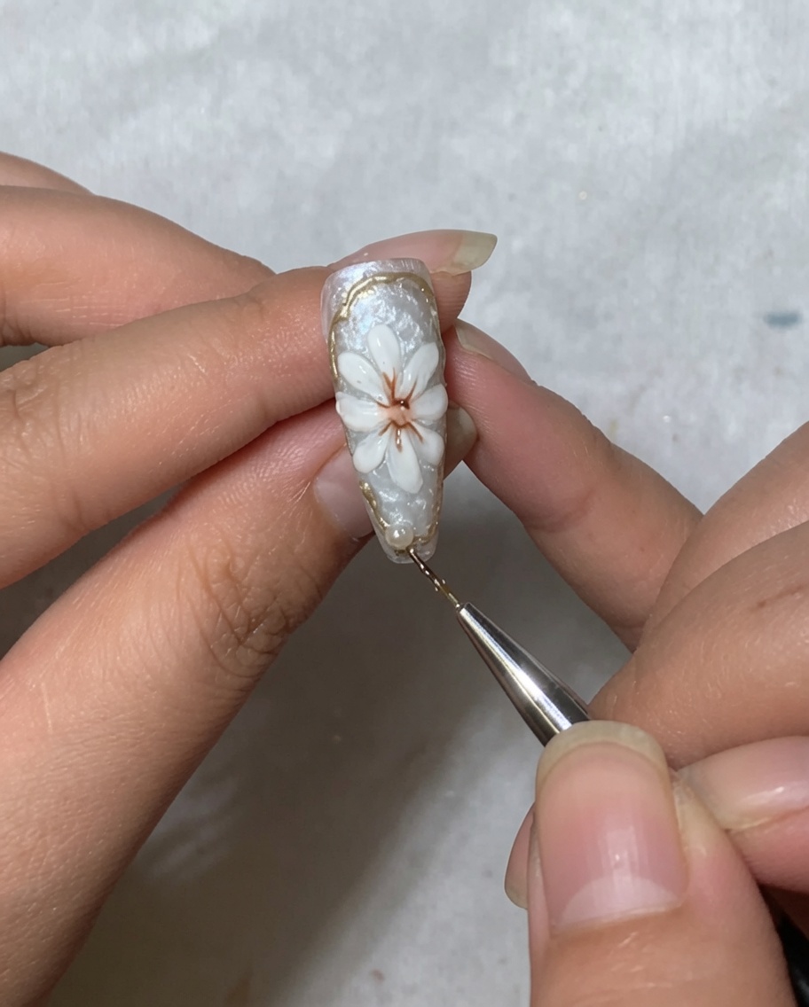 Ein Nagelkunst-Werkzeug platziert eine kleine weiße Perle im Nagelhautbereich eines mit einem Gänseblümchen verzierten Nagels.