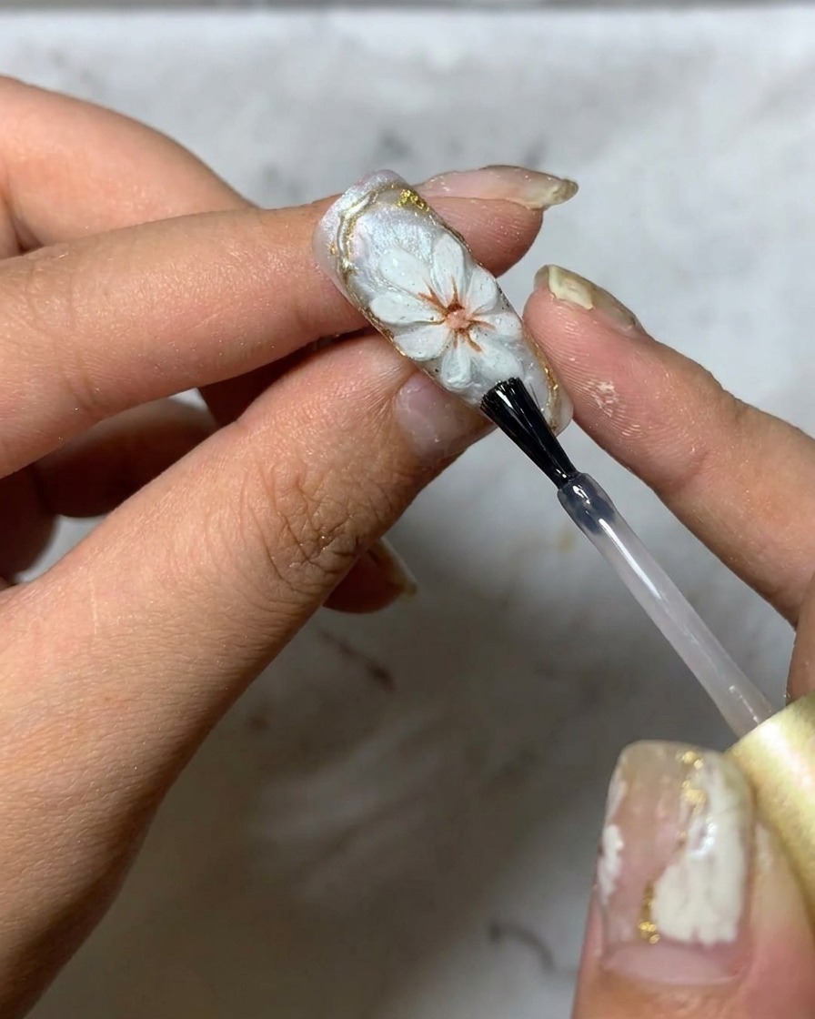Ein Pinsel trägt ein letztes glänzendes Top Coat über das 3D-Gänseblümchen-Nageldesign auf.