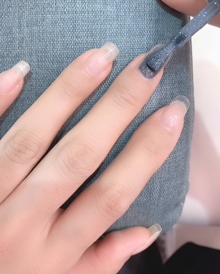 Eine Nahaufnahme eines Pinsels, der hellgraues Gel-Polish auf einen vorbereiteten Fingernagel aufträgt.