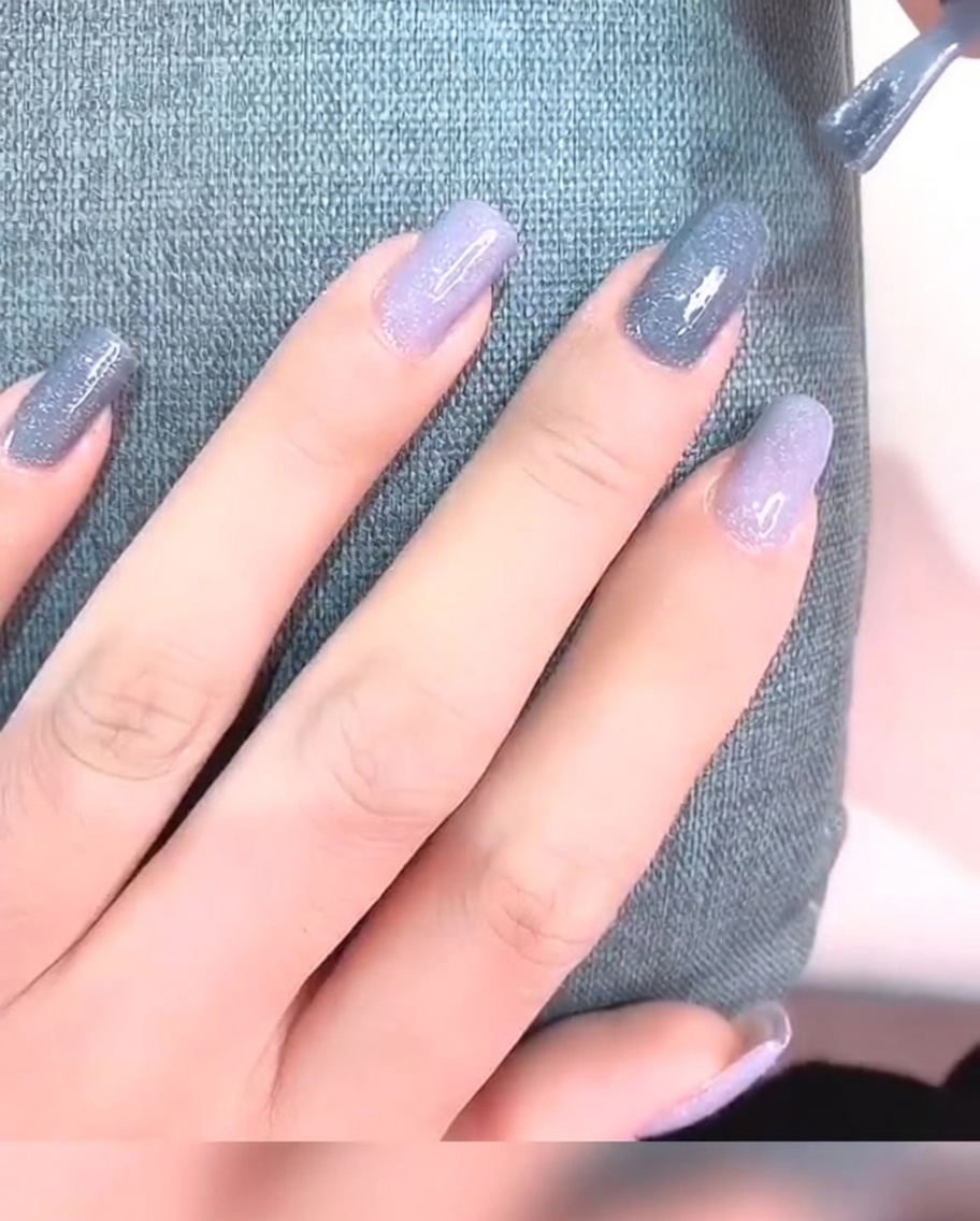 Eine Nahaufnahme eines Fingernagels mit zwei Schichten grauem Gel-Lack, der nun deckend und glatt aussieht.