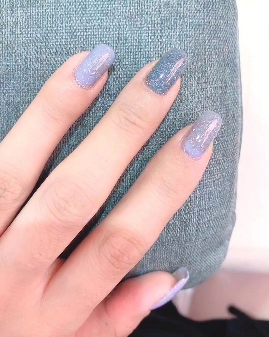 Eine Hand hält einen Fine-Liner-Pinsel und malt weiße Gänseblümchen-Blütenblätter auf einen grau lackierten Nagel.
