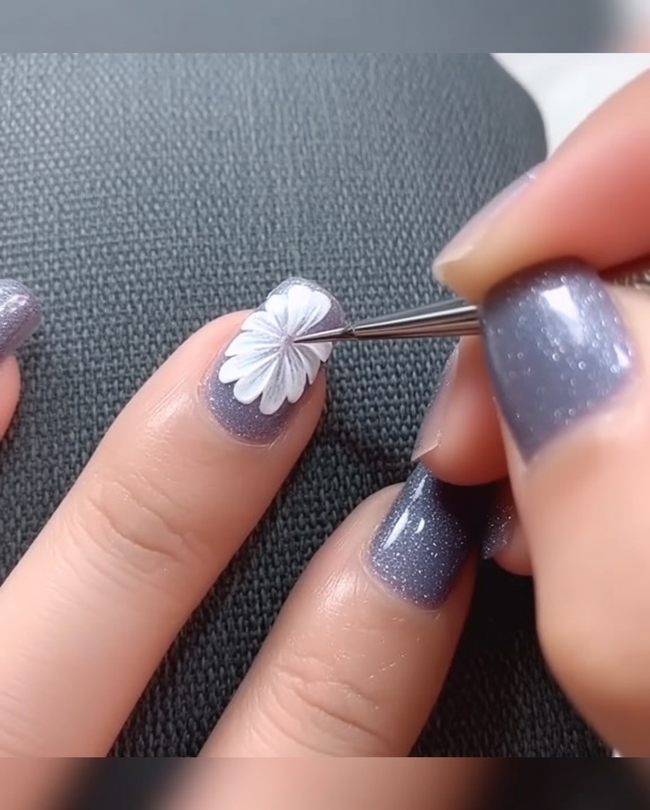 Eine Nahaufnahme eines Fine-Liner-Pinsels, der einen kleinen Punkt schwarzer Gel-Farbe in die Mitte eines weißen Gänseblümchens auf grauer Basis setzt.