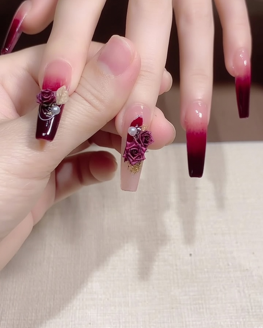 Eine Pinzette platziert eine kleine Perle und ein goldenes Metallelement neben einem Rosen-Charm auf einem Fingernagel.