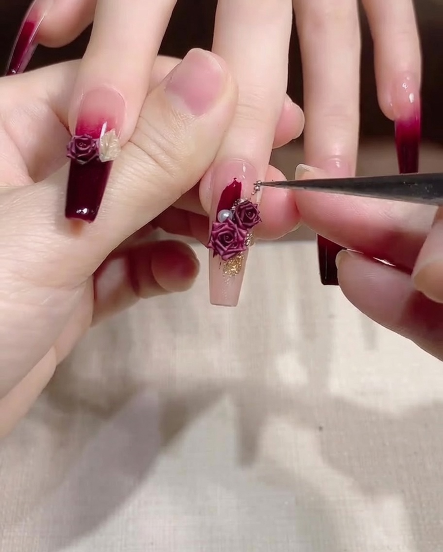 Ein feiner Detailpinsel wird genutzt, um kleine Gold- und Perlendekorationen auf einem Fingernagel zu korrigieren.