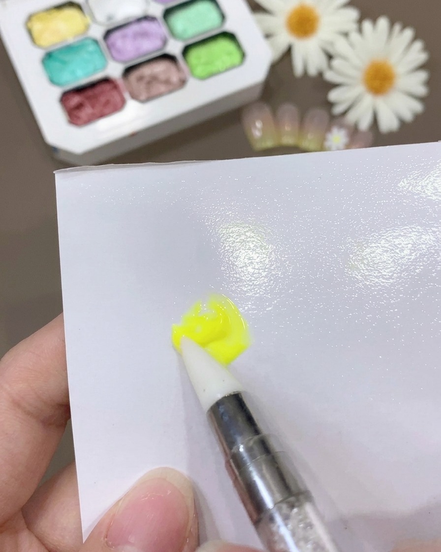 Ein Pinsel vermischt gelbes Gel und Base Coat auf einer weißen Oberfläche zu einer dünnen, konsistenten Mischung.