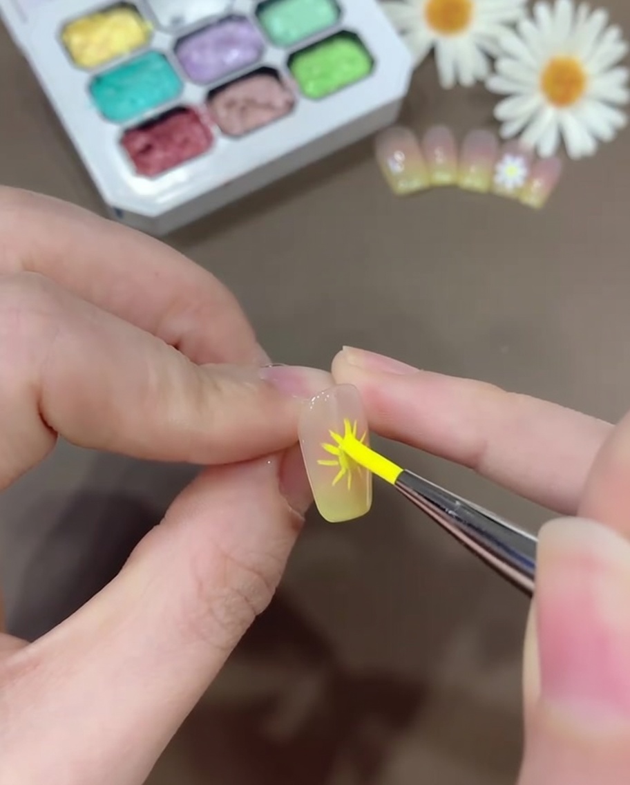 Ein Nailart-Pinsel trägt weißes Gel auf, um abgerundete, gänseblümchenartige Blütenblätter über den markierten Hilfslinien zu formen.