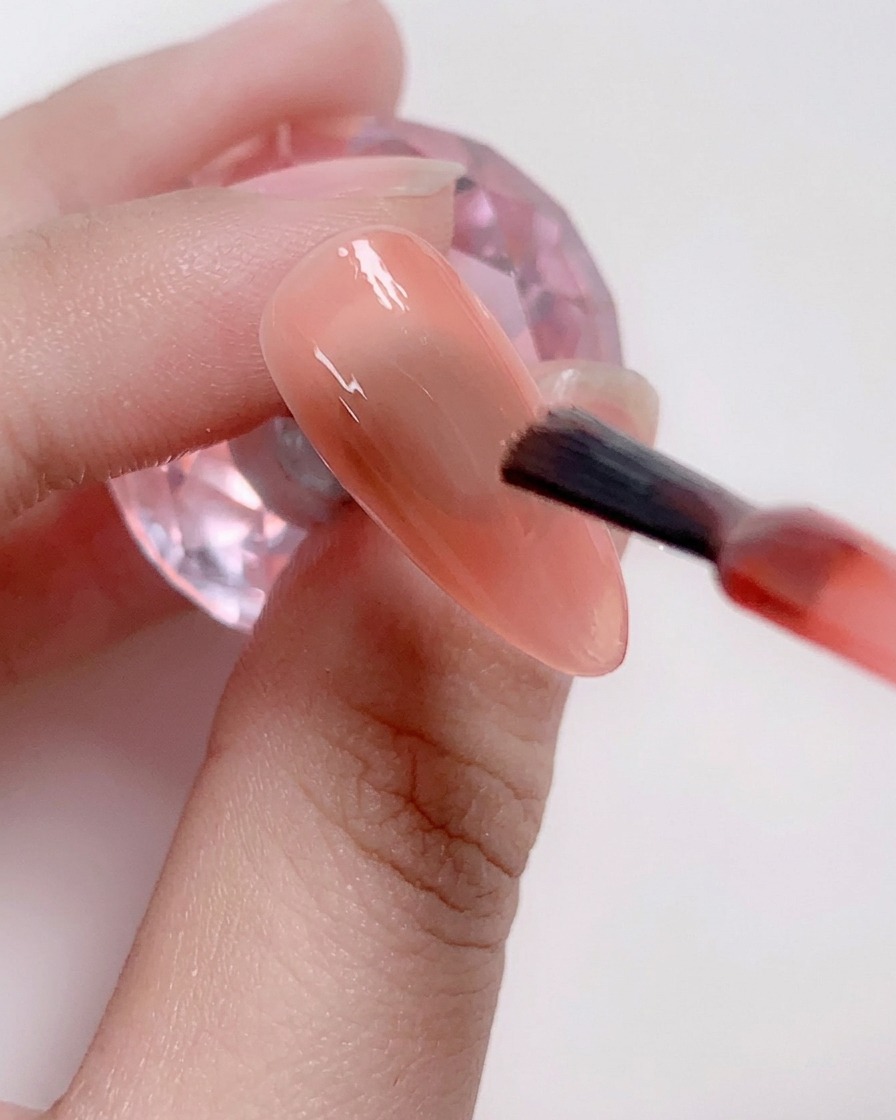 Ein Pinsel trägt ein hellrosa Farbgel auf die Nagelmitte auf.
