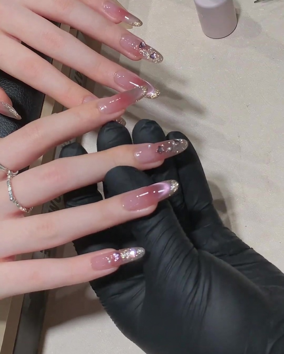 Ein Pinsel trägt ein glänzendes Top Coat über einem fertigen Nageldesign mit Strasssteinen auf.