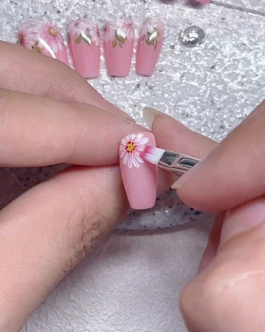 Ein flacher Pinsel, der sanft die Kanten der weißen Blütenblätter auf einem rosa Nagel verblendet.