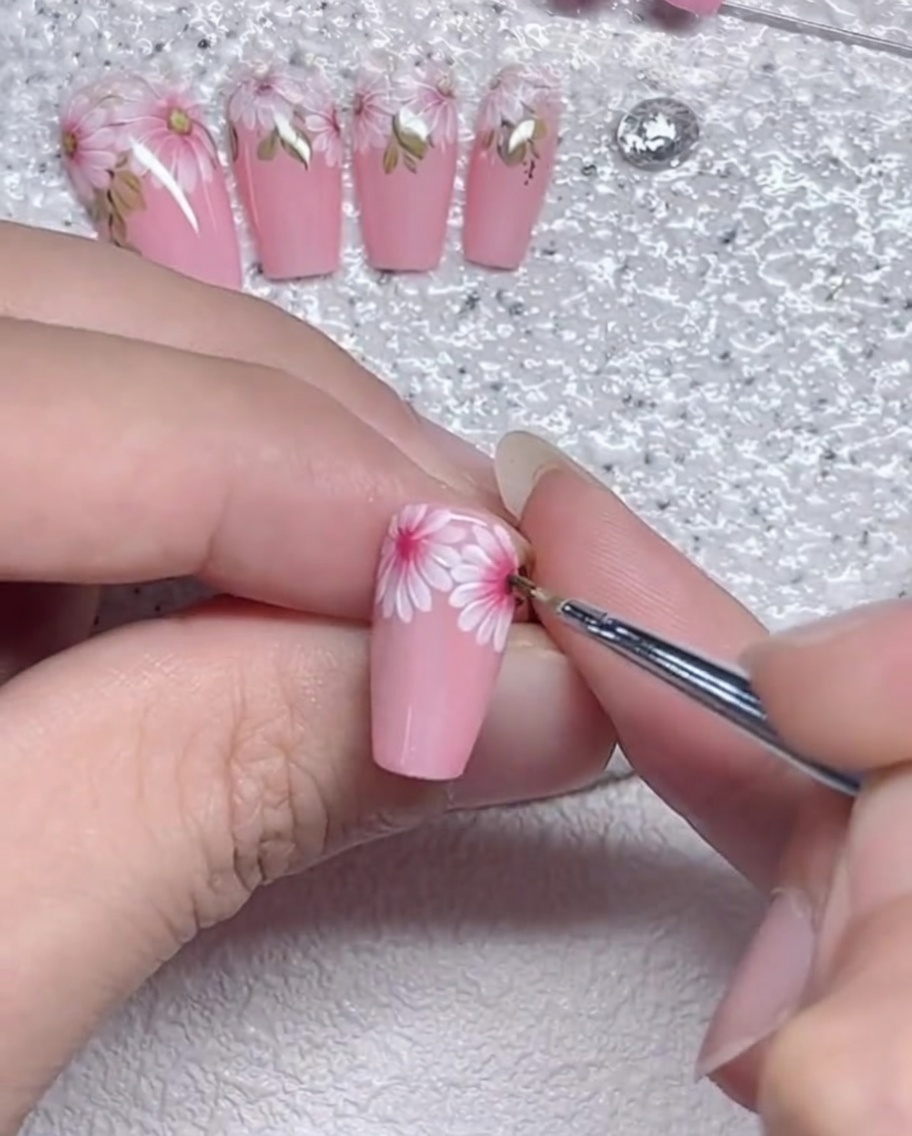 Nahaufnahme eines feinen Liner-Pinsels, der die Kanten der Gänseblümchen-Blütenblätter auf einem Nagel verfeinert.