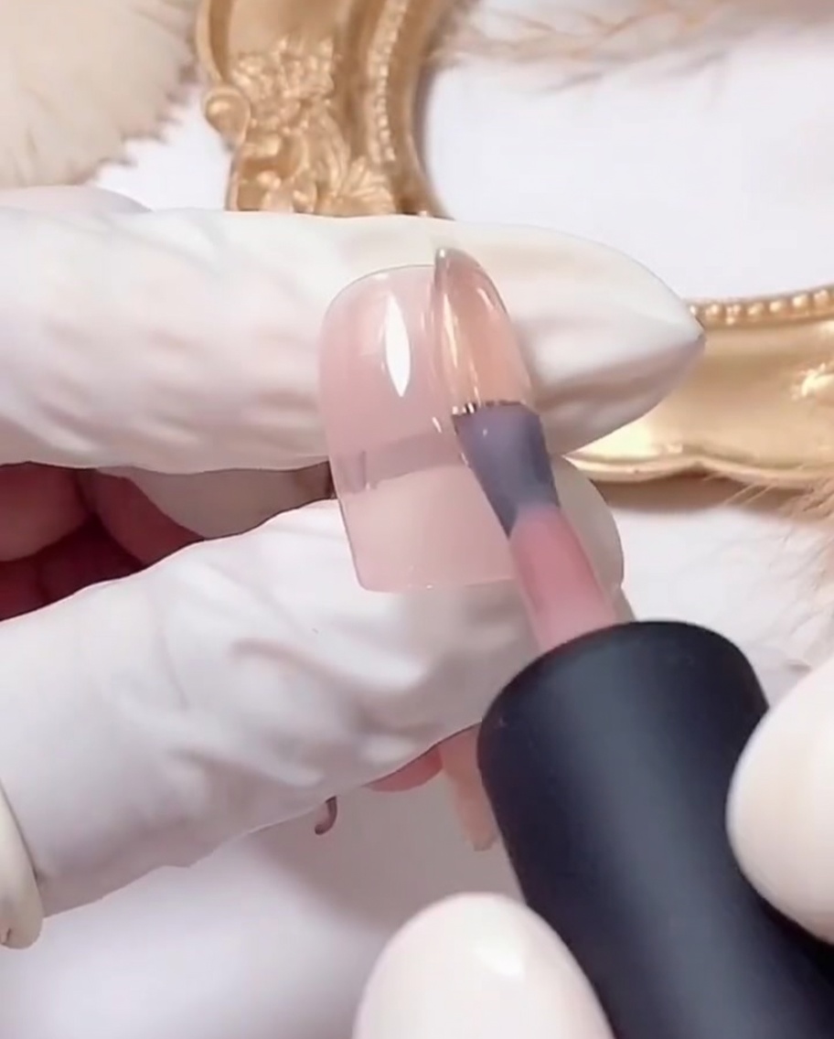Ein flacher Gelpinsel beim Auftragen von silbernem Glitzergel auf die Spitze eines rosa beschichteten Nagels.