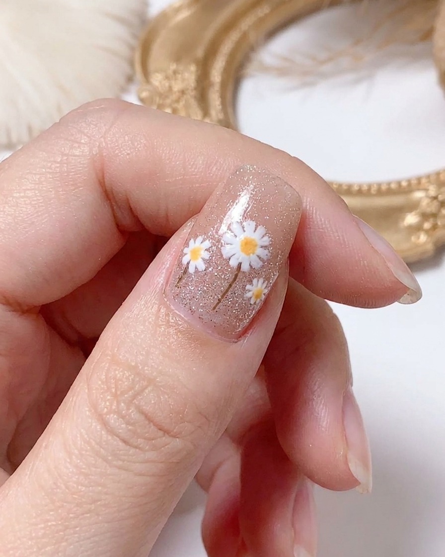 Eine Hand härtet das fertige Gänseblümchen-Nageldesign unter einer Lampe aus.