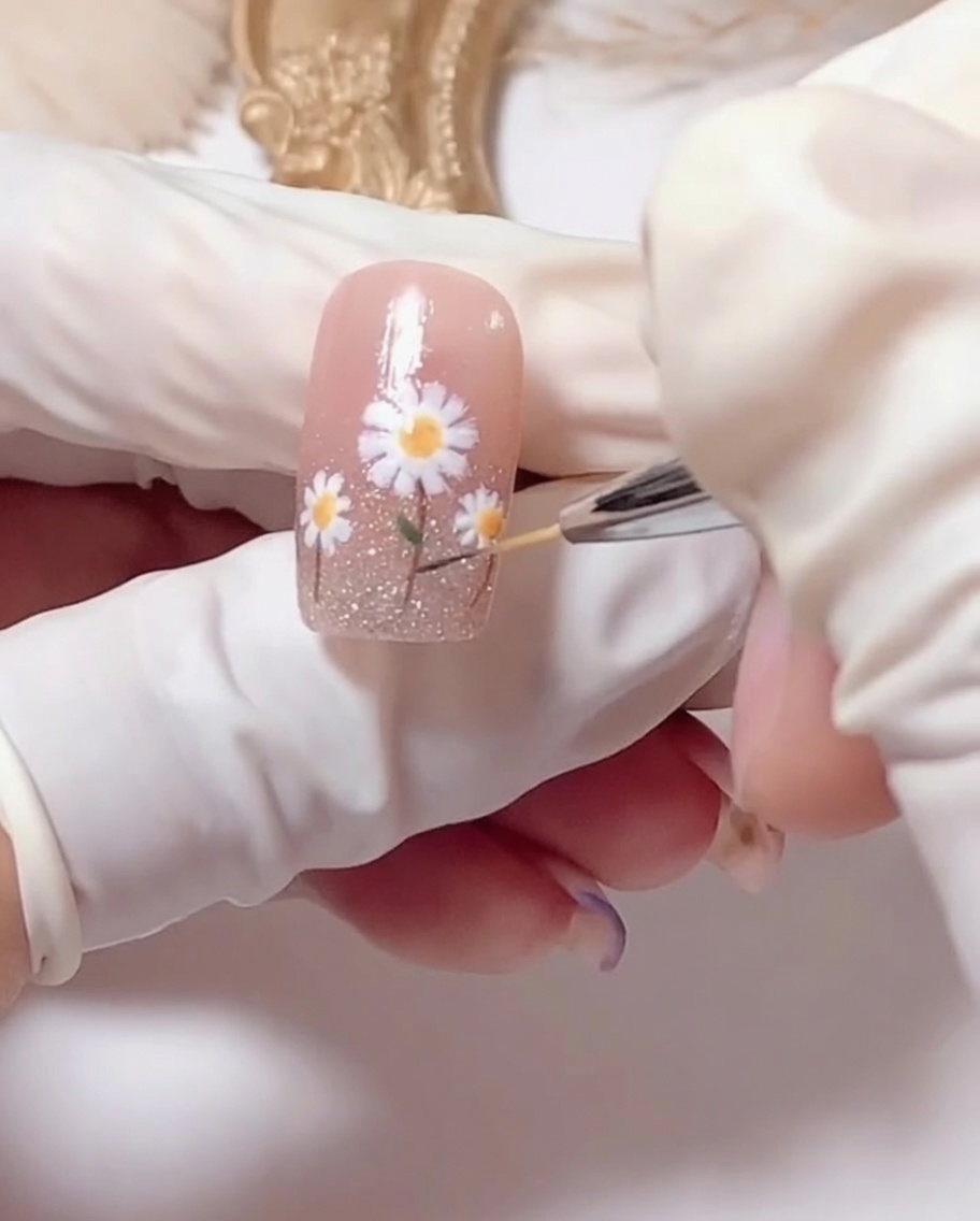Ein Pinsel beim Auftragen von klarem, glänzendem Überlack über das fertige Gänseblümchen-Nageldesign.