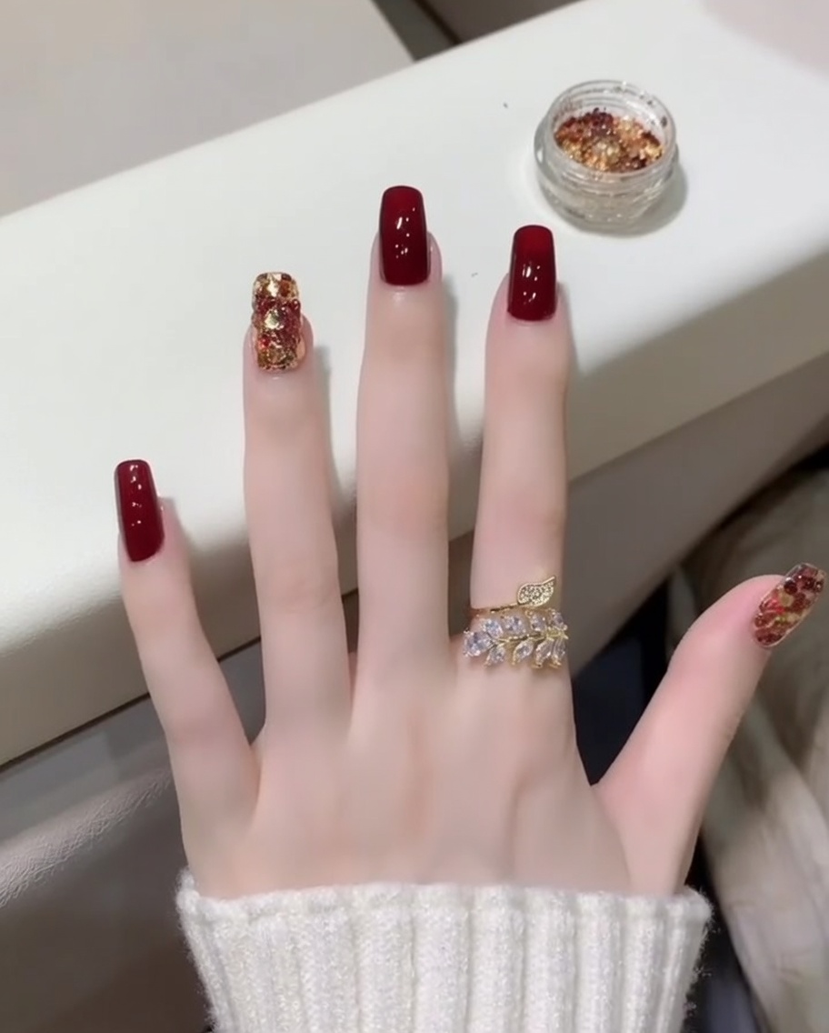 Ein Pinsel trägt einen klaren Top Coat über die roten und glitzernden Nägel auf.