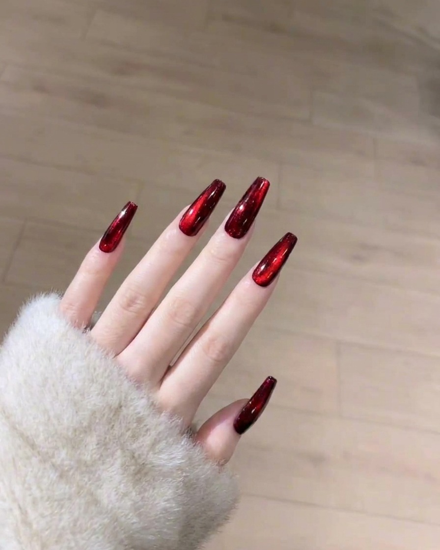 Ein Pinsel trägt eine glatte, klare Schicht glänzenden Überlacks auf den ausgehärteten roten Cat-Eye-Nagel auf.