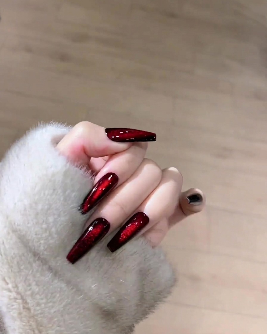 Eine Hand hält ein fusselfreies Tuch und reinigt die Oberfläche eines dunklen rubinroten Cat-Eye-Nagels.
