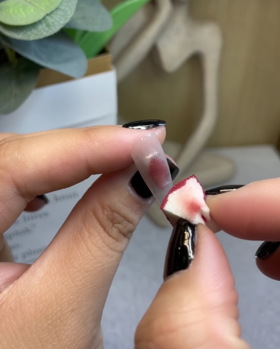 Ein Make-up-Schwamm tupft weinrotes Gel auf die Mitte eines klaren Nagel-Tips.