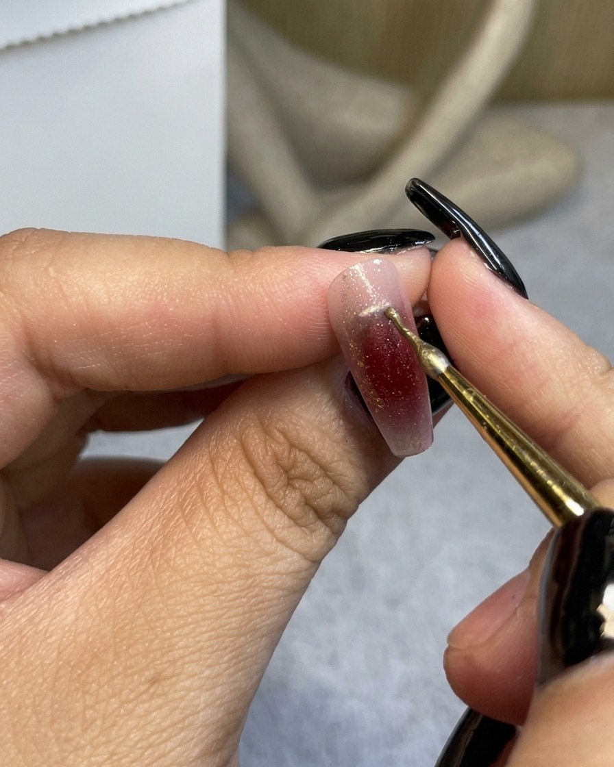 Ein feiner Pinsel zieht eine dünne goldene Linie in der Nähe der Nagelhaut.