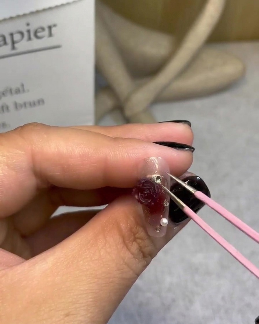 Mit einer Pinzette werden letzte Perlen um die 3D-Rose arrangiert.