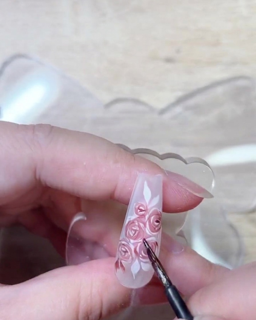 Eine Pinsel-Detailaufnahme zeigt tiefrotes Gel, das aufgetragen wird, um die Schatten und die Struktur der Rosenblüten zu betonen.