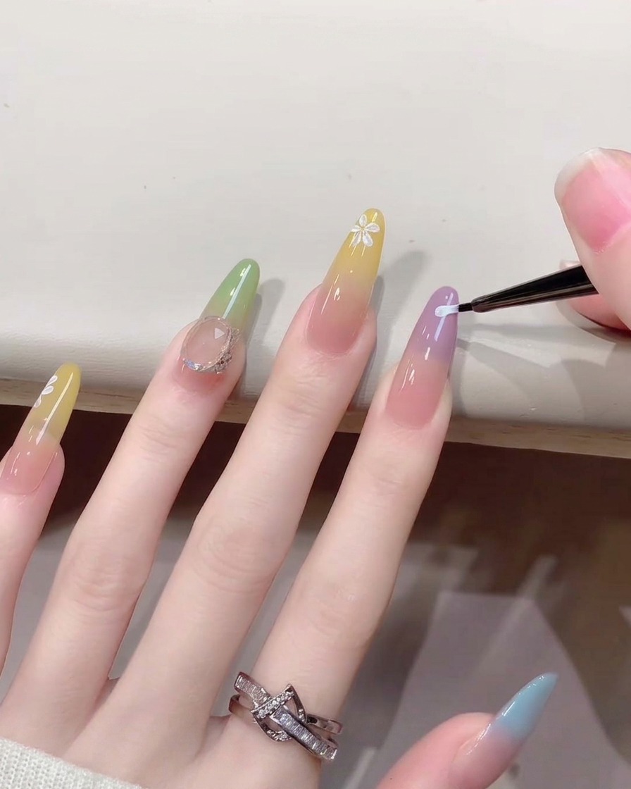 Nahaufnahme eines feinen Nagelkunst-Pinsels, der kleine weiße Blütenblätter auf einen Nagel mit Farbverlauf malt.