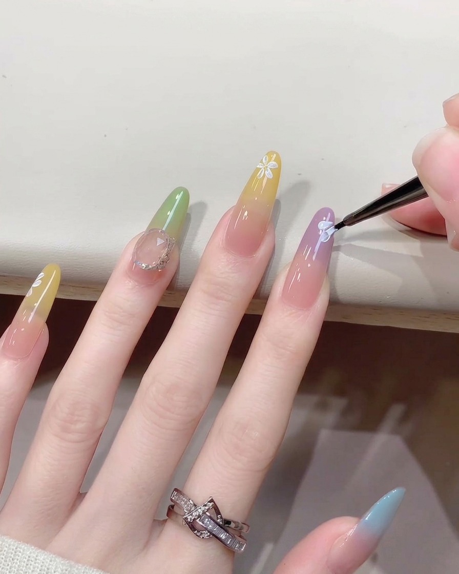 Nahaufnahme eines feinen Pinsels, der kleine weiße Punkte in die Mitte eines gemalten Blumen-Nageldesigns setzt.