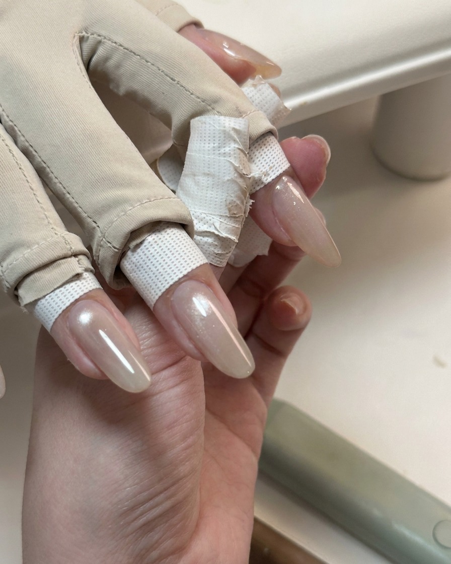 Eine Hand zeigt lange Nägel, die mit einer glänzenden, durchscheinenden Cat-Eye-Gelschicht bedeckt sind.