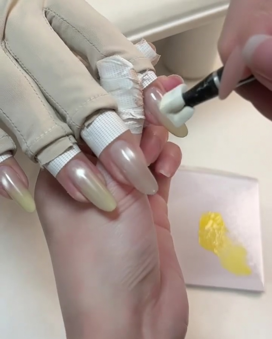 Ein Spezialwerkzeug tupft gelbes Gel auf die Spitze eines Nude-Cat-Eye-Nagels, um einen Farbverlauf zu starten.