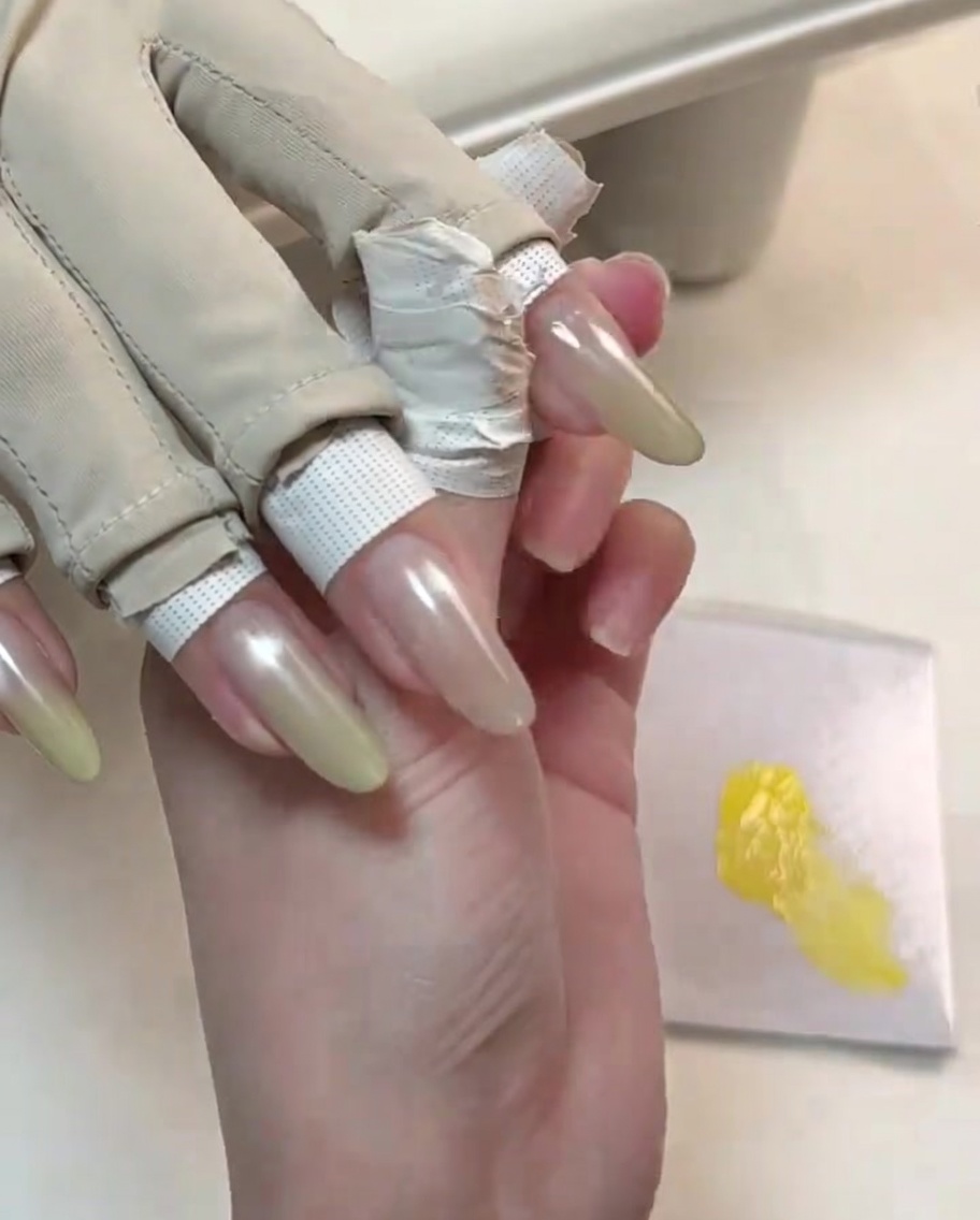 Ein Werkzeug verfeinert die zweite Schicht gelben Gels auf der Spitze eines manikürten Nagels für einen helleren Farbverlauf.
